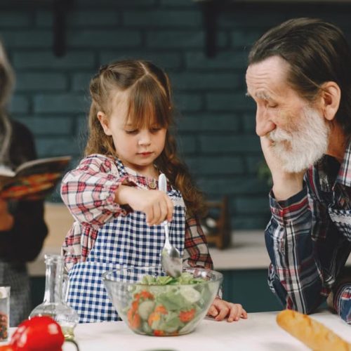 Grandfather and granddaughter making salad while grandmother reads a recipe.