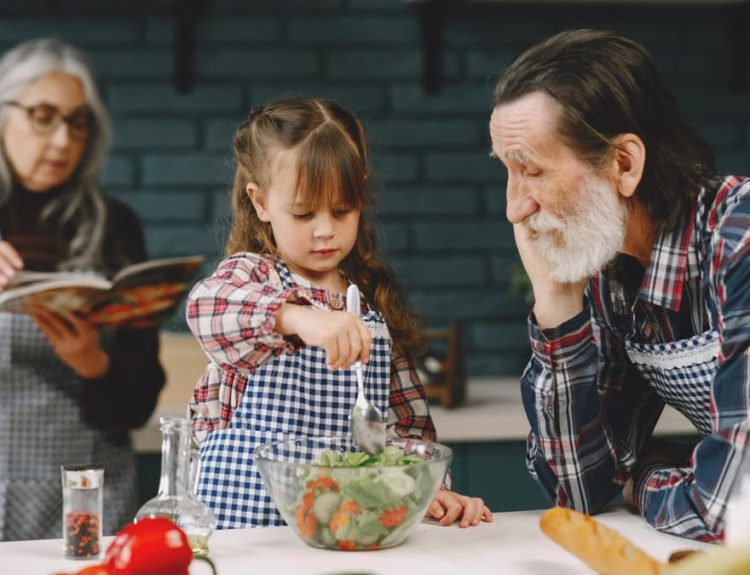 Grandfather and granddaughter making salad while grandmother reads a recipe.